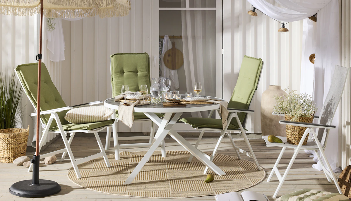 Ett runt bord med vitt underrede och fyra matchande stolar med gröna dynor står på ett trädäck.