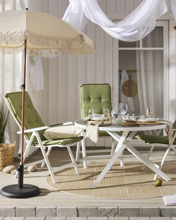 Ett runt bord med vitt underrede och fyra matchande stolar med gröna dynor står på ett trädäck.