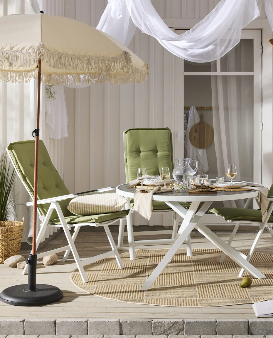 Ett runt bord med vitt underrede och fyra matchande stolar med gröna dynor står på ett trädäck.