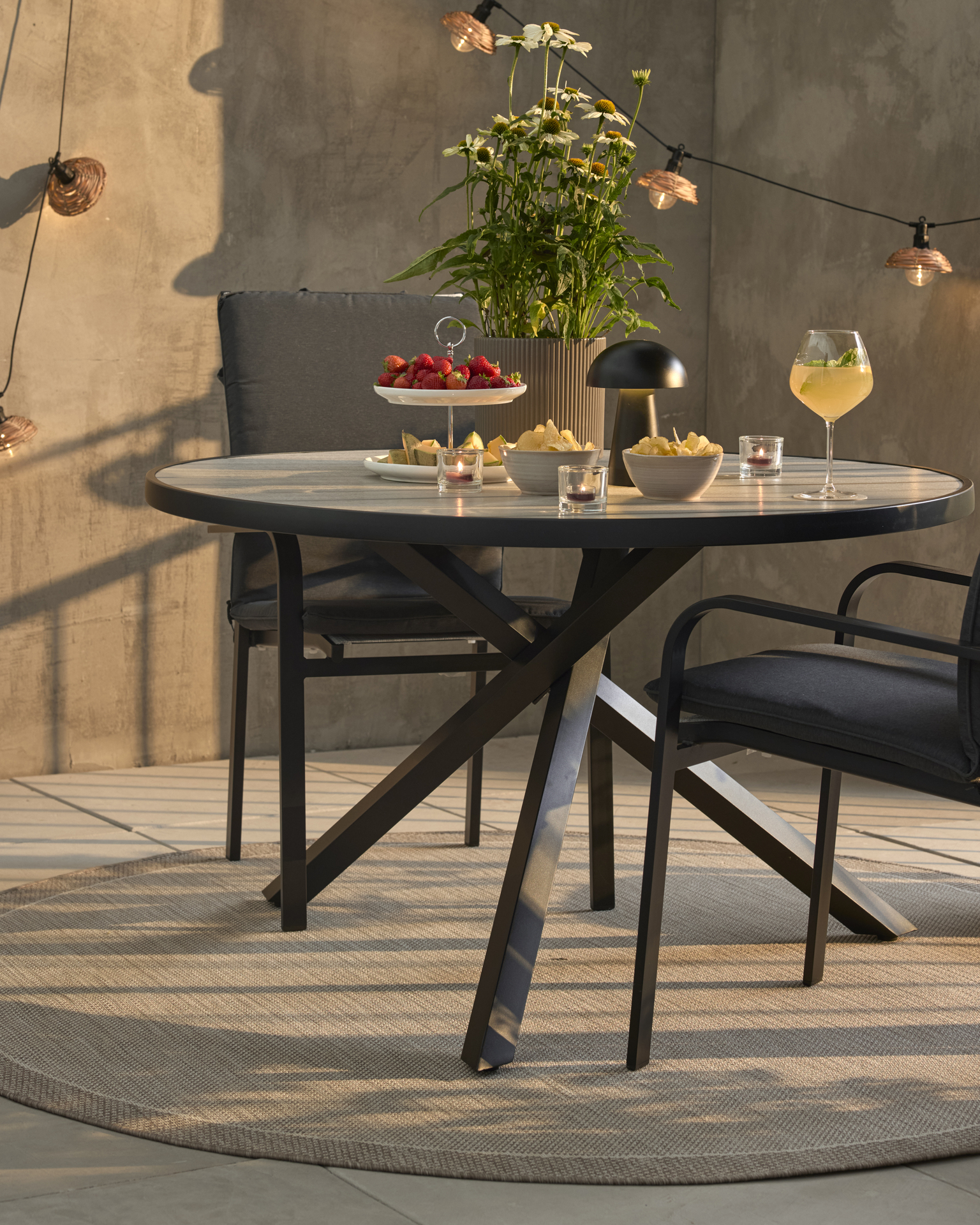 Ett runt bord med svart underrede och två svarta stolar med svarta dynor står på ett trädäck.