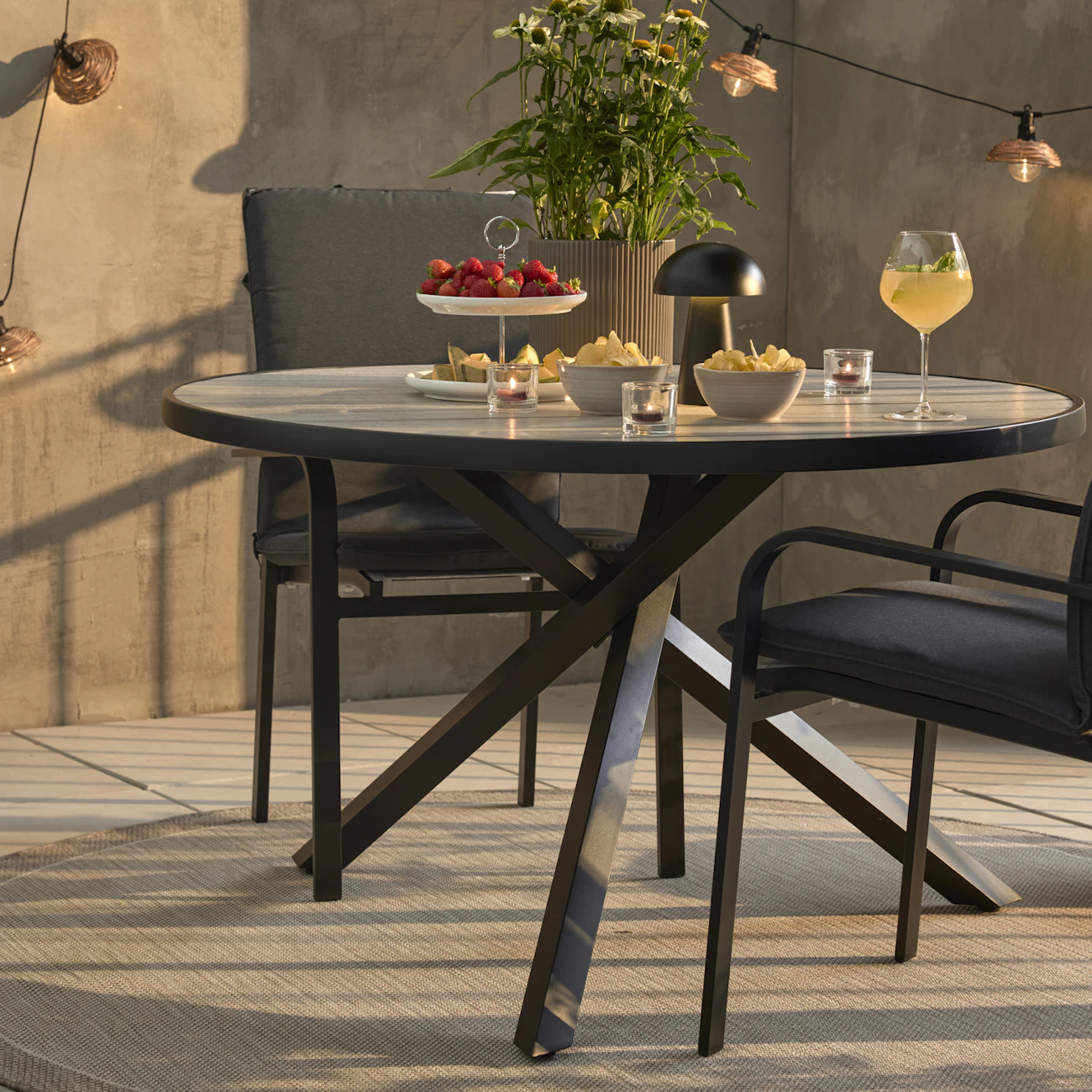 Ett runt bord med svart underrede och två svarta stolar med svarta dynor står på ett trädäck.
