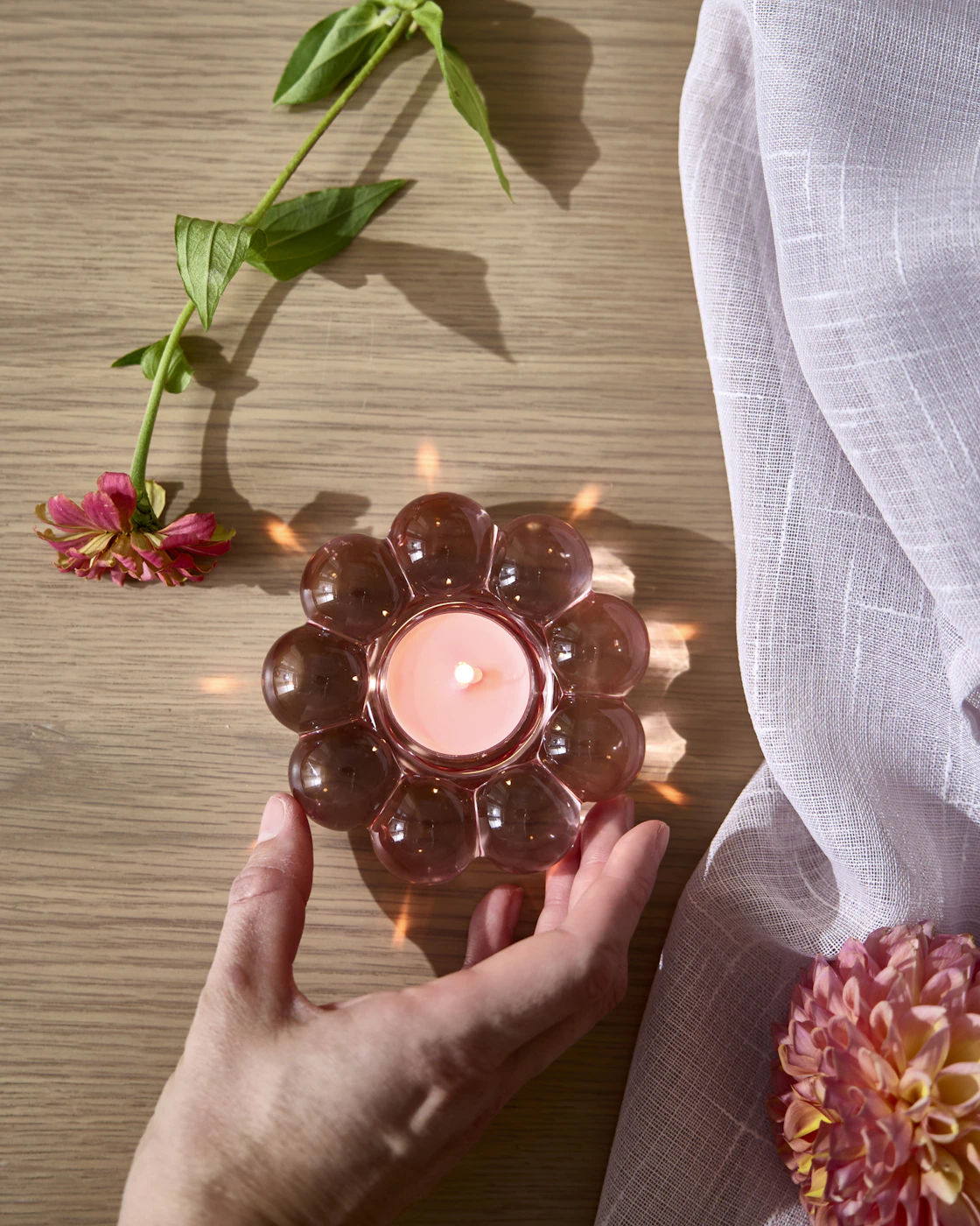 En hand håller i en rosa blomformad ljuslykta.