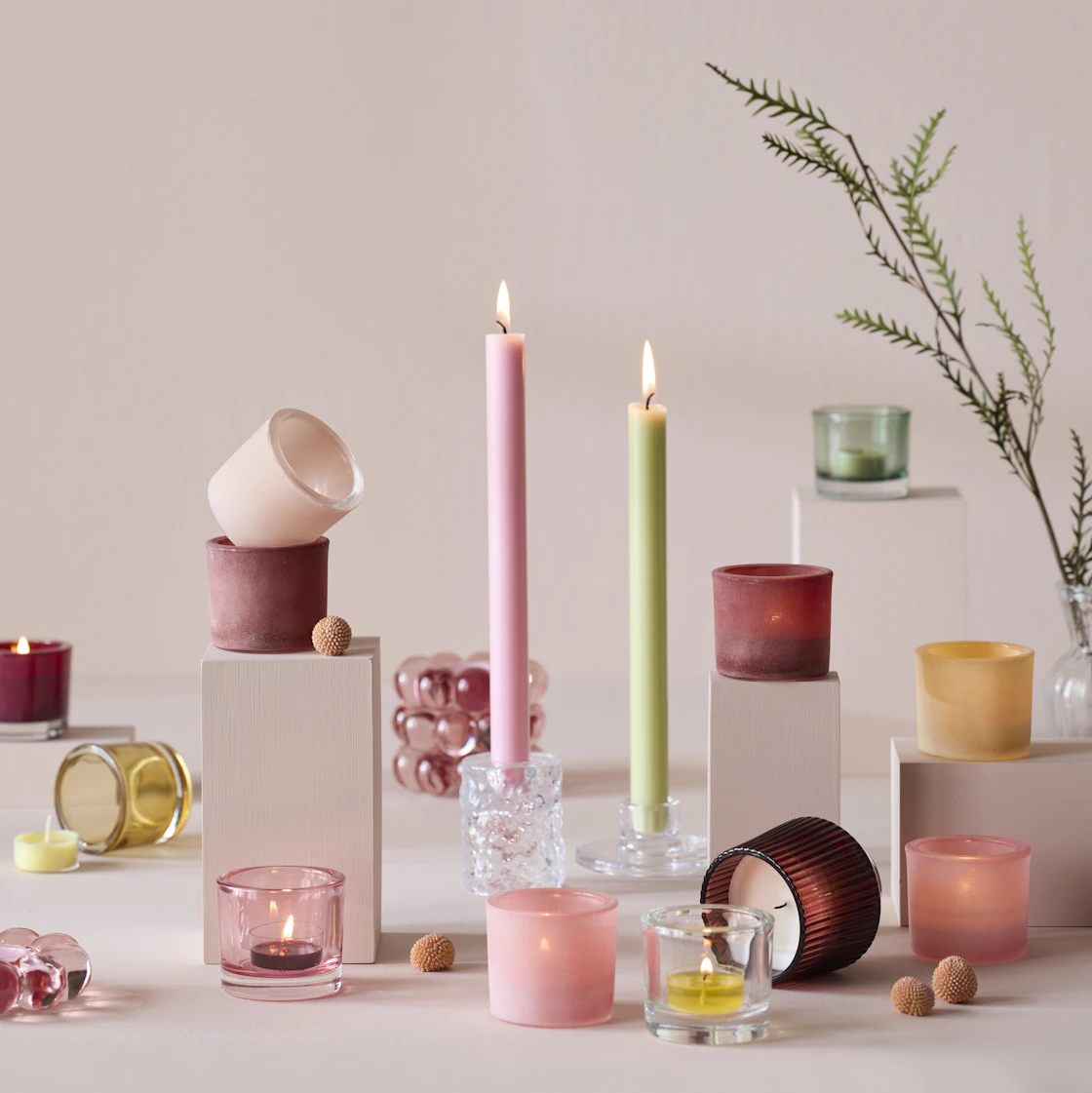 Flera ljuslyktor och ljuslyktor i olika färger och former står framför en rosa bakgrund.