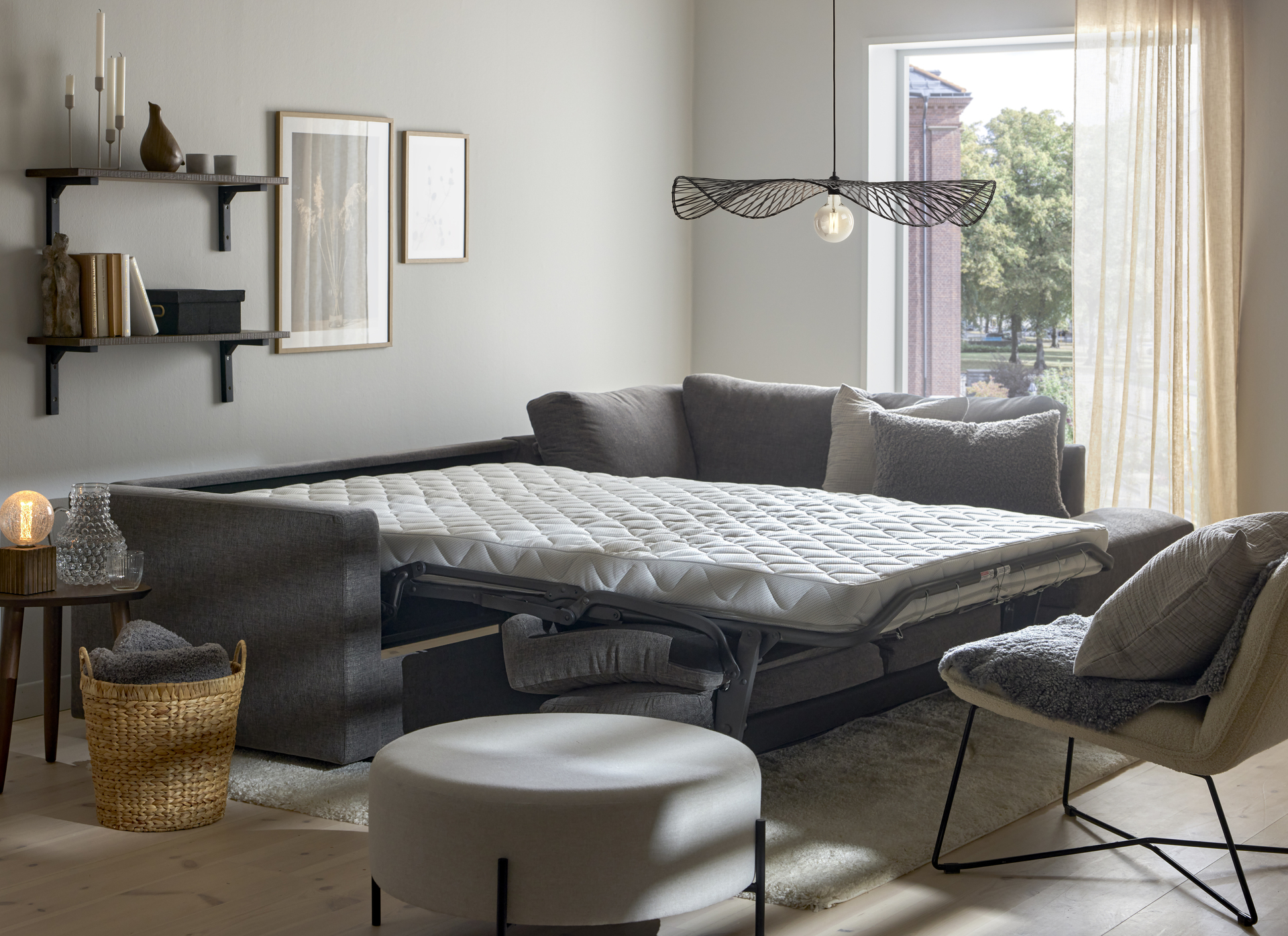 I ett vitt rum står en grå bäddsoffa med madrass utbäddad