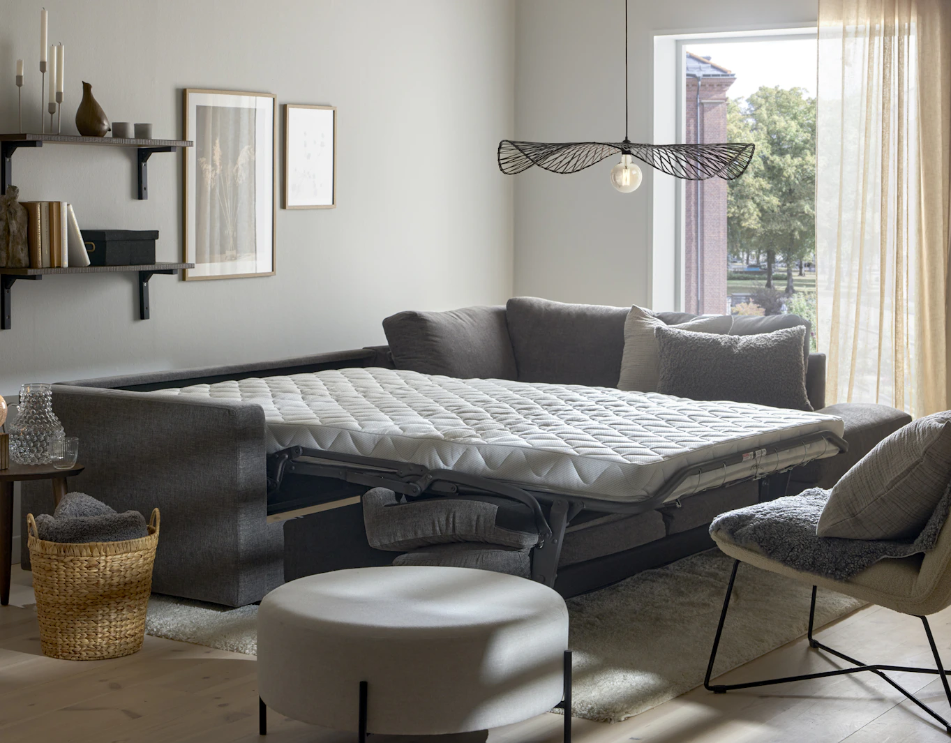 I ett vitt rum står en grå bäddsoffa med madrass utbäddad