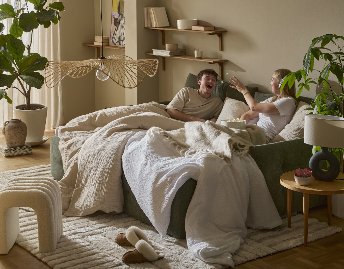 I en grön bäddsoffa sitter en tjej och en kille nedbäddade under ett täcke och kastar popcorn till varandra