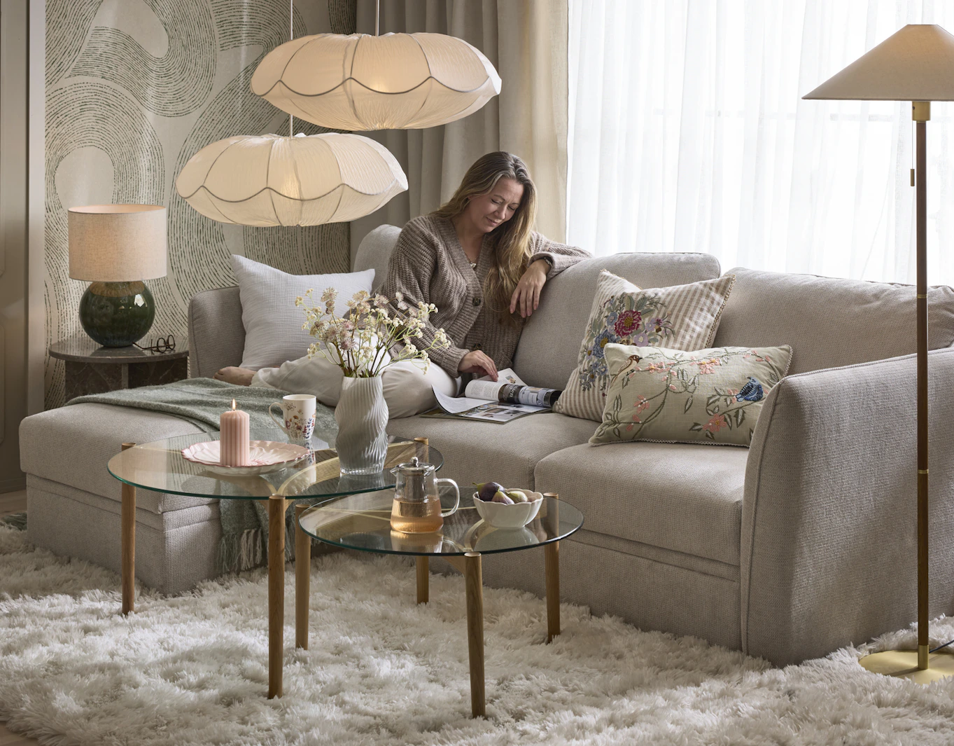 I en grå soffa sitter en kvinna och läser en tidning