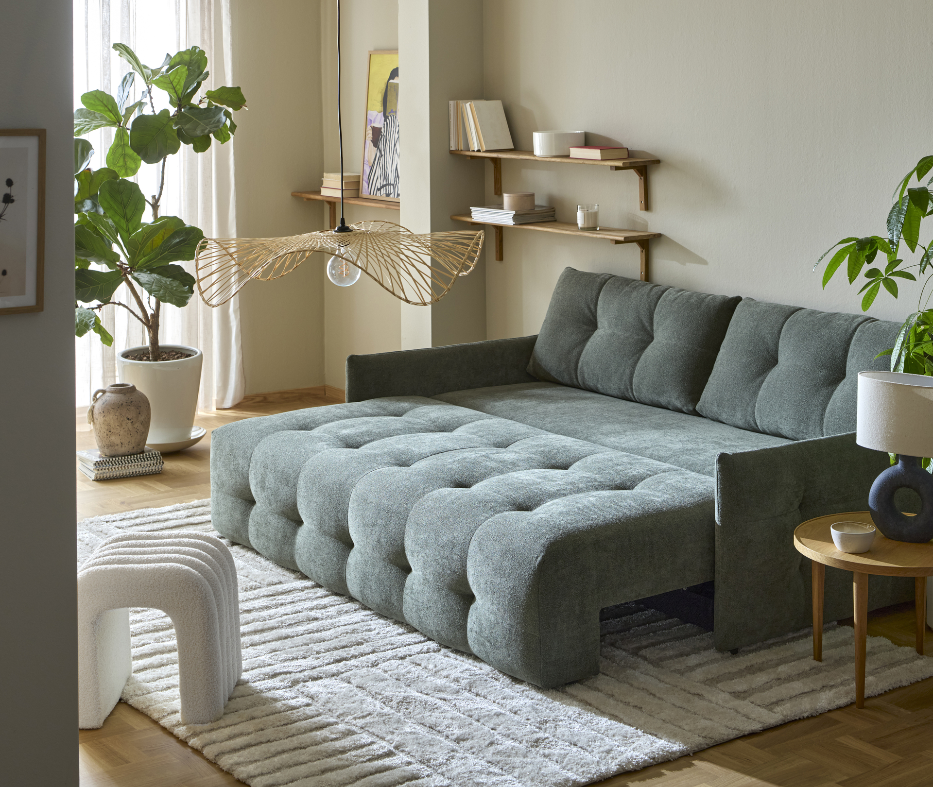 En grön bäddsoffa som är klädd runt om står utbäddad i ett gult vardagsrum