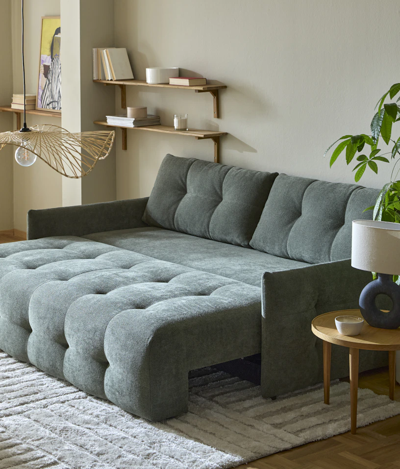 En grön bäddsoffa som är klädd runt om står utbäddad i ett gult vardagsrum