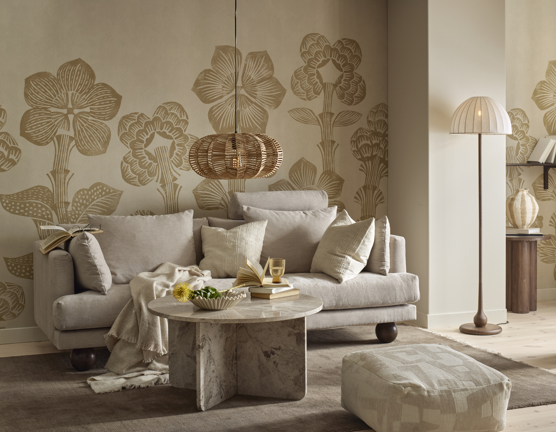 I ett vardagsrum med mönstrad, beige tapet står en beige soffa med klotformade ben