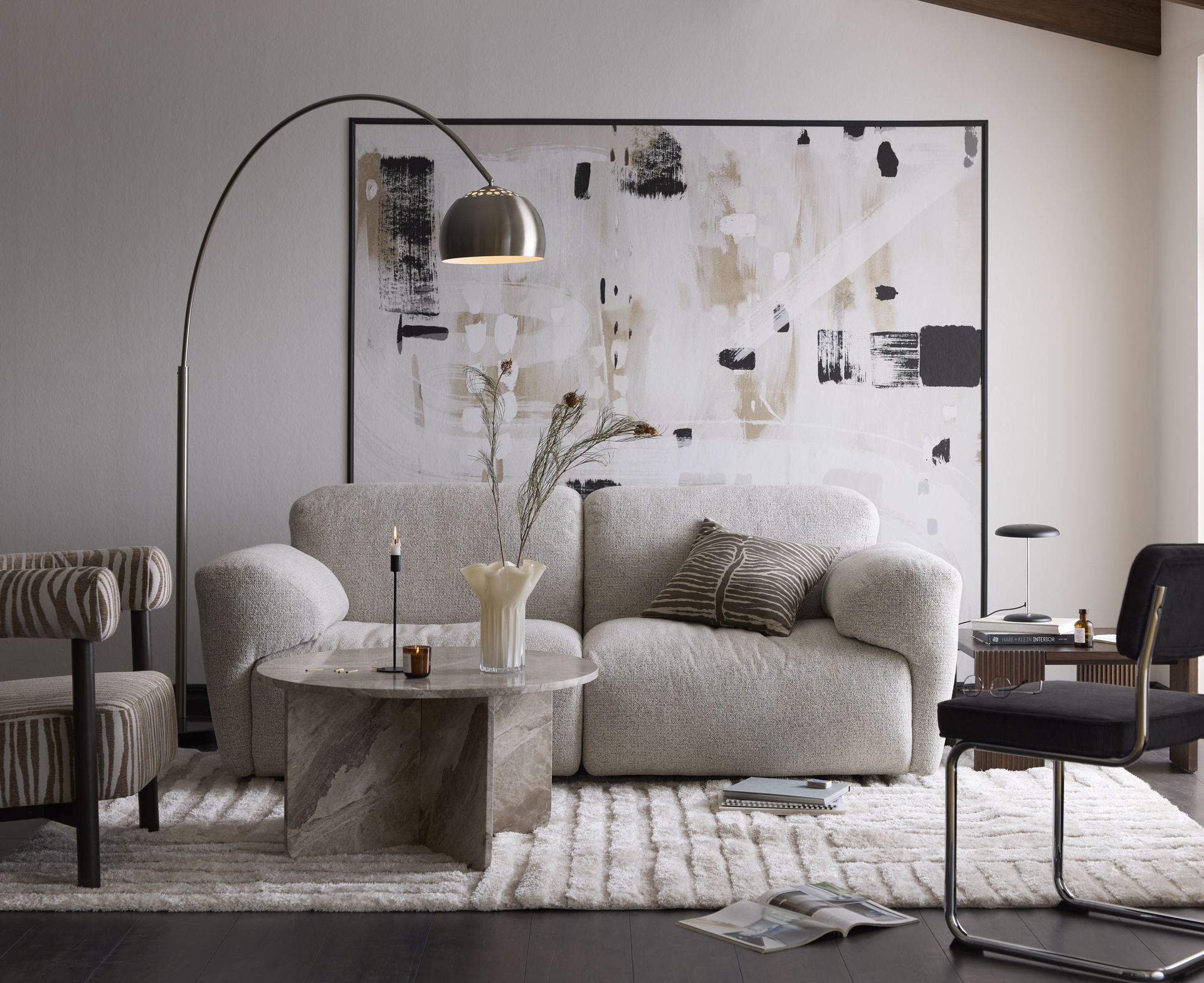 I ett vardagsrum i neutrala toner med svarta accenter står en beige soffa bakom ett soffbord i marmor