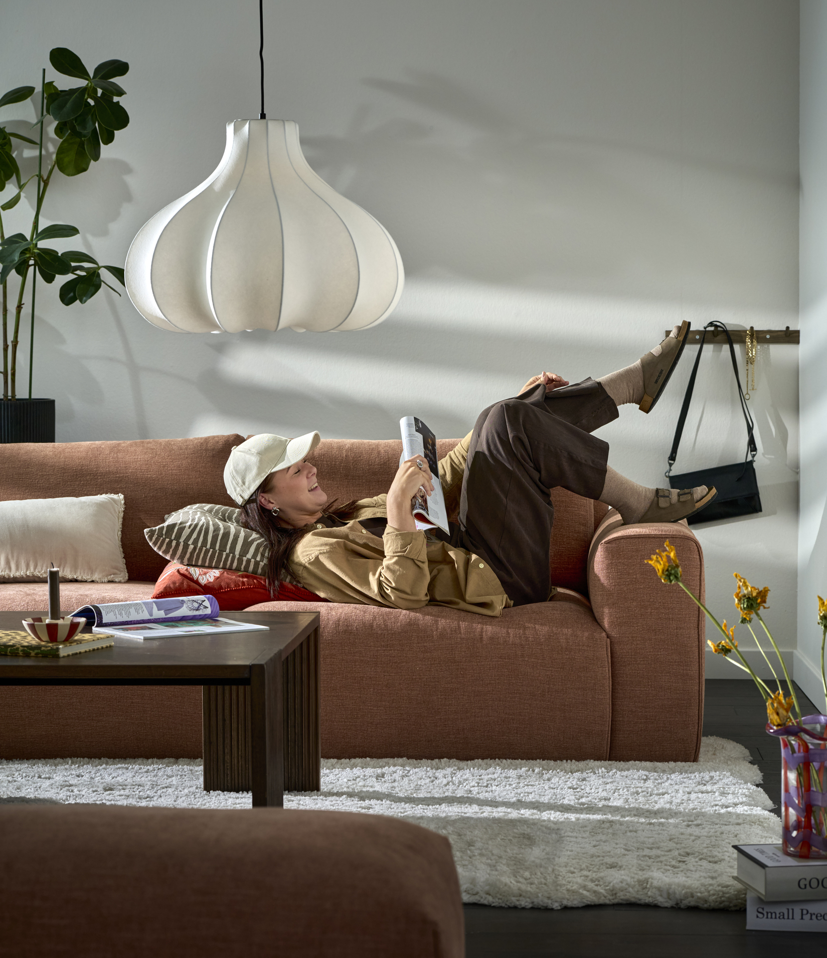 I en rostfärgad Free soffa ligger en ung kvinna på rygg och läser ett magasin medans hennes fötter dinglar över kanten.