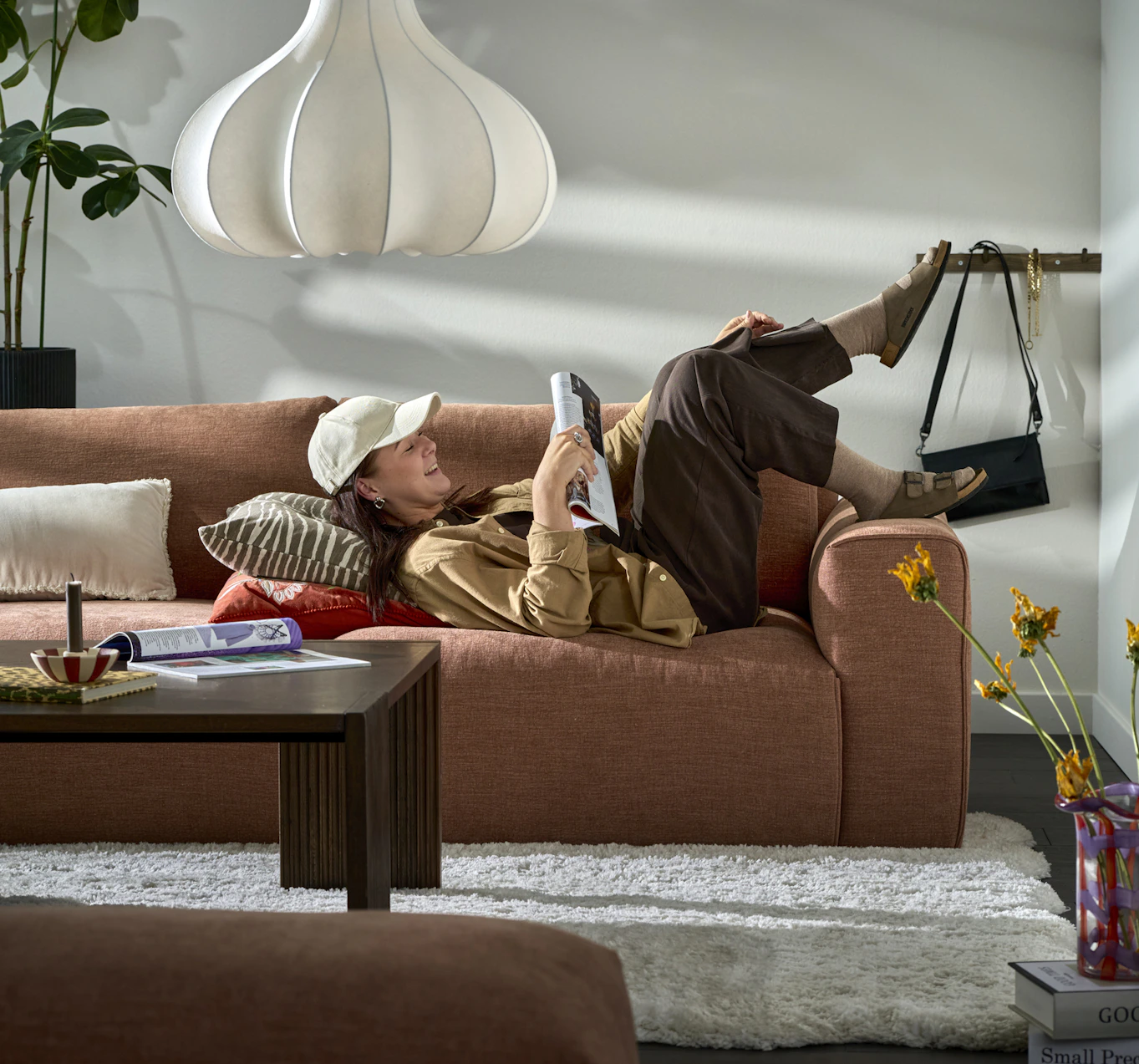 I en rostfärgad Free soffa ligger en ung kvinna på rygg och läser ett magasin medans hennes fötter dinglar över kanten.
