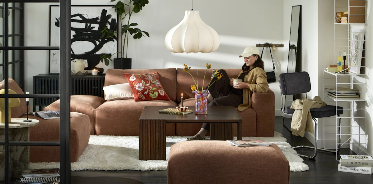 I en rostfärgad soffa sitter en ung kvinna och läser ett magasin