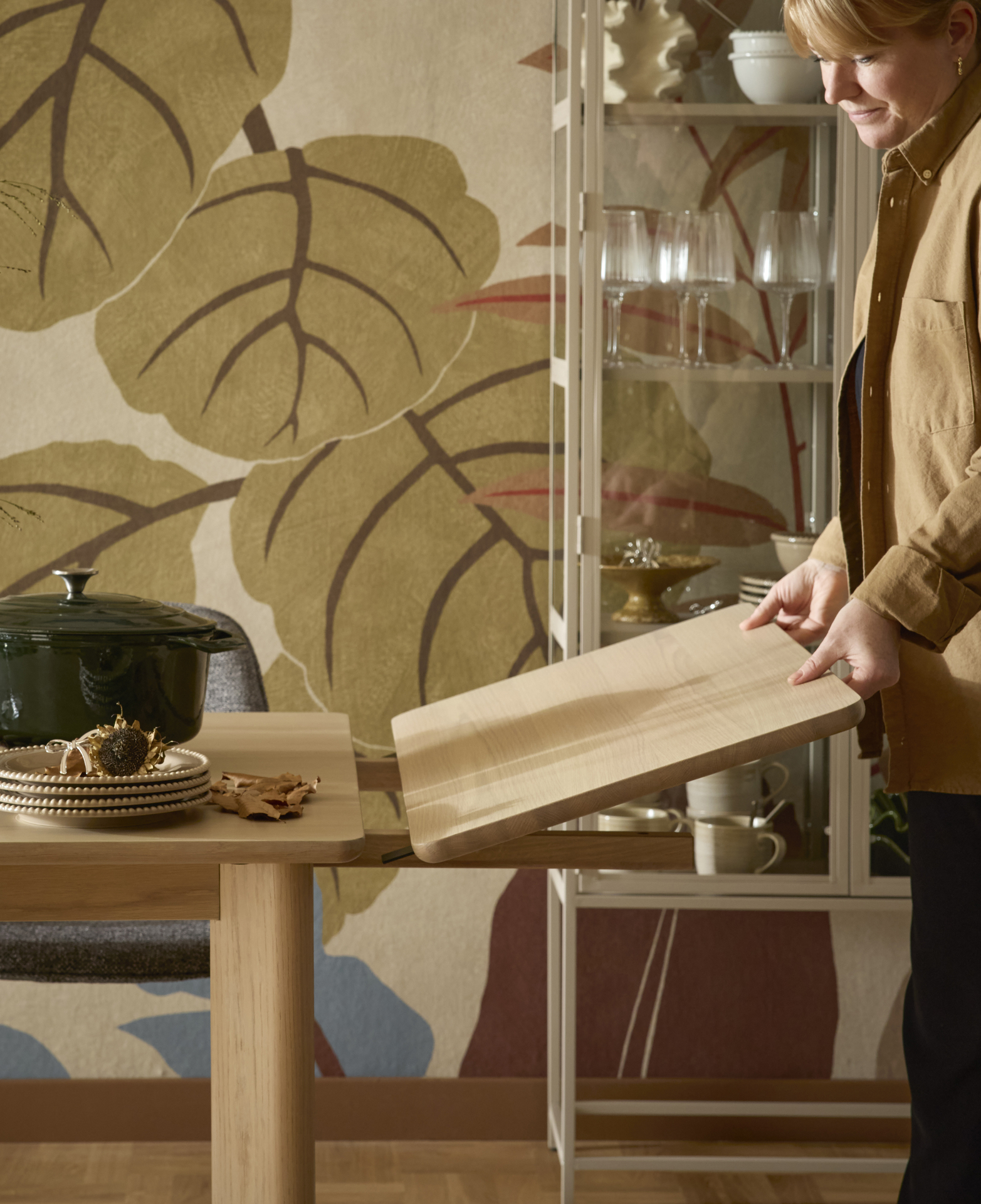 En kvinna sätter fast en tilläggsskiva på ett matbord i ljust trä.