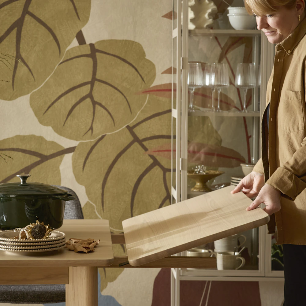 En kvinna sätter fast en tilläggsskiva på ett matbord i ljust trä.