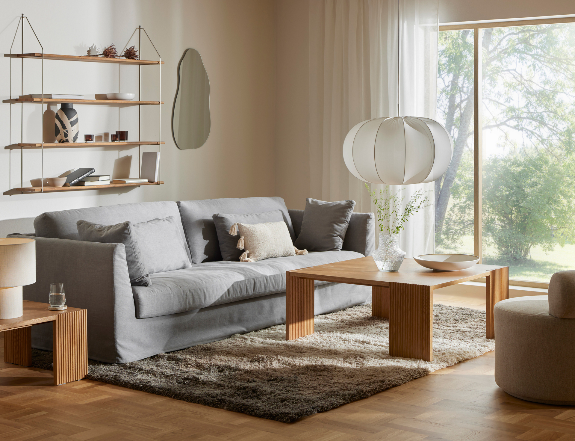 I ett vardagsrum i beige ton står en ljusgrå soffa med kappa