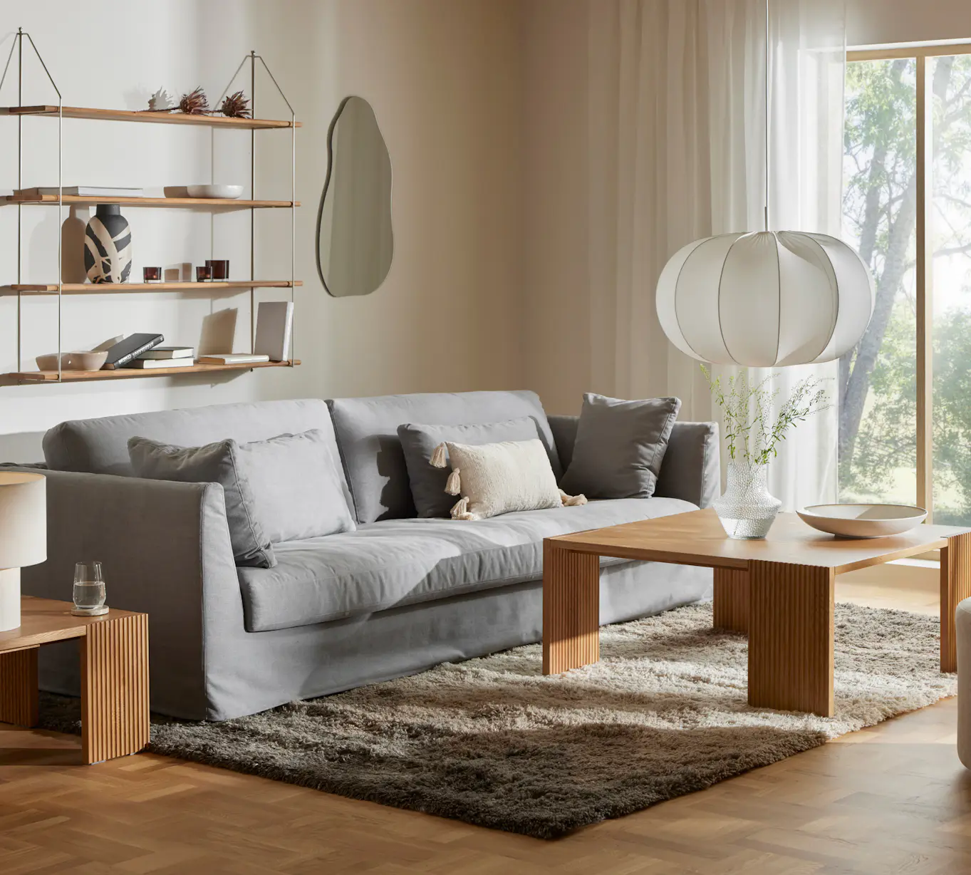 I ett vardagsrum i beige ton står en ljusgrå soffa med kappa