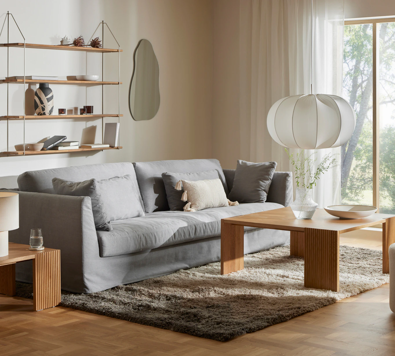 I ett vardagsrum i beige ton står en ljusgrå soffa med kappa