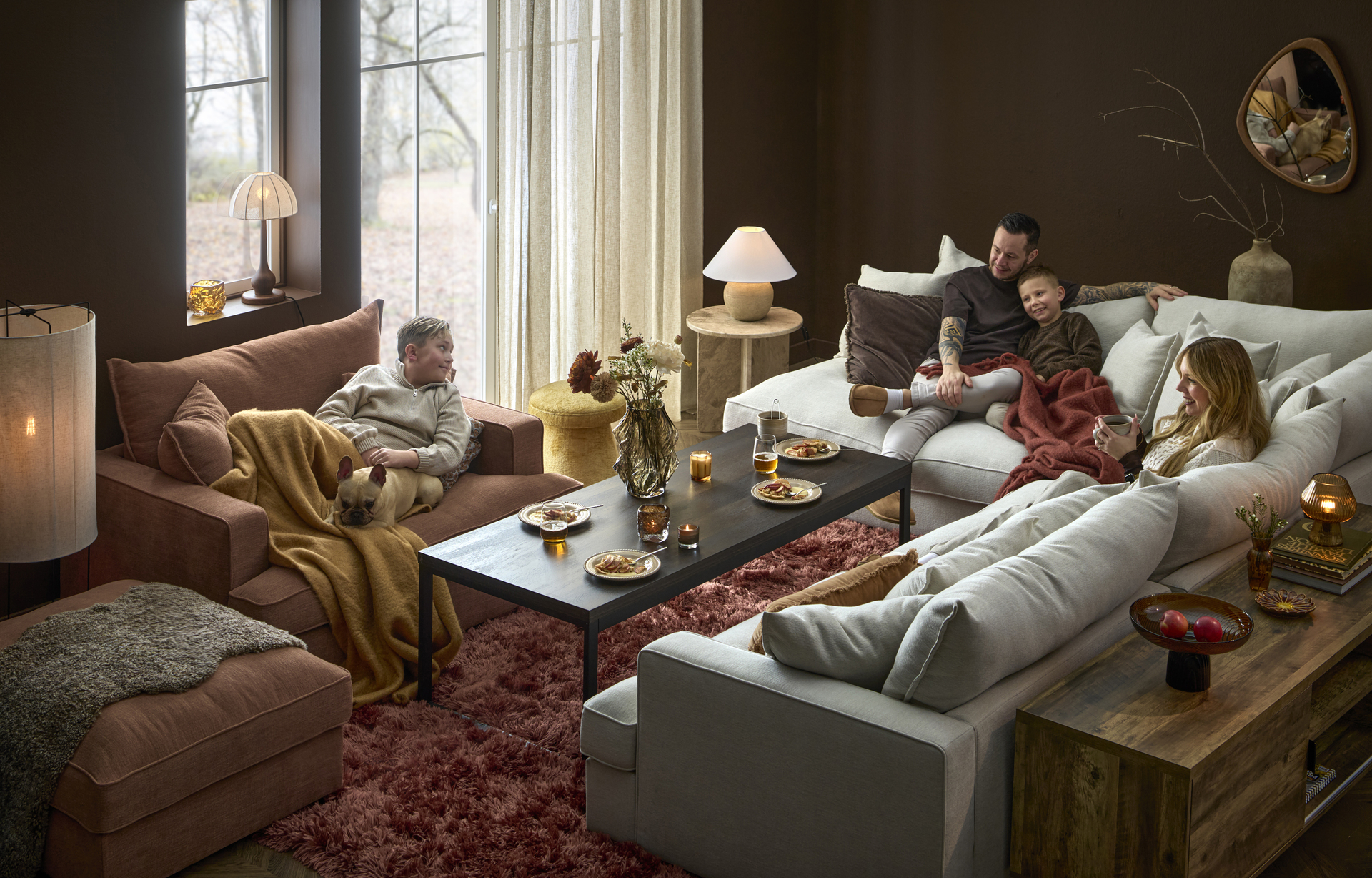 I en stor, djup Rossi soffa sitter en familj med två barn och en hund och myser