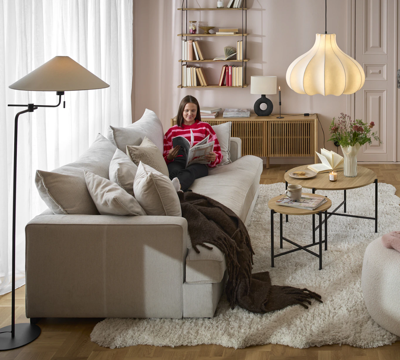 En kvinna sitter i en beige soffa i ett ljusrosa vardagsrum