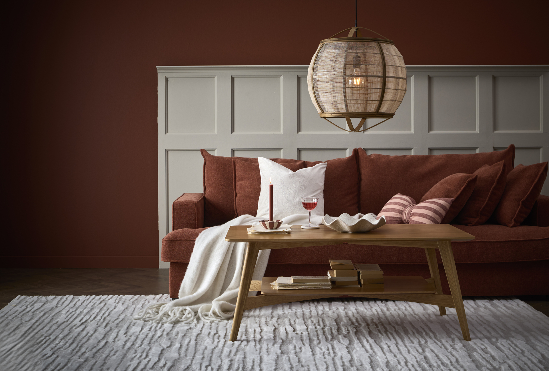 I ett vardagsrum står en roströd Mila soffa bakom ett soffbord i ek