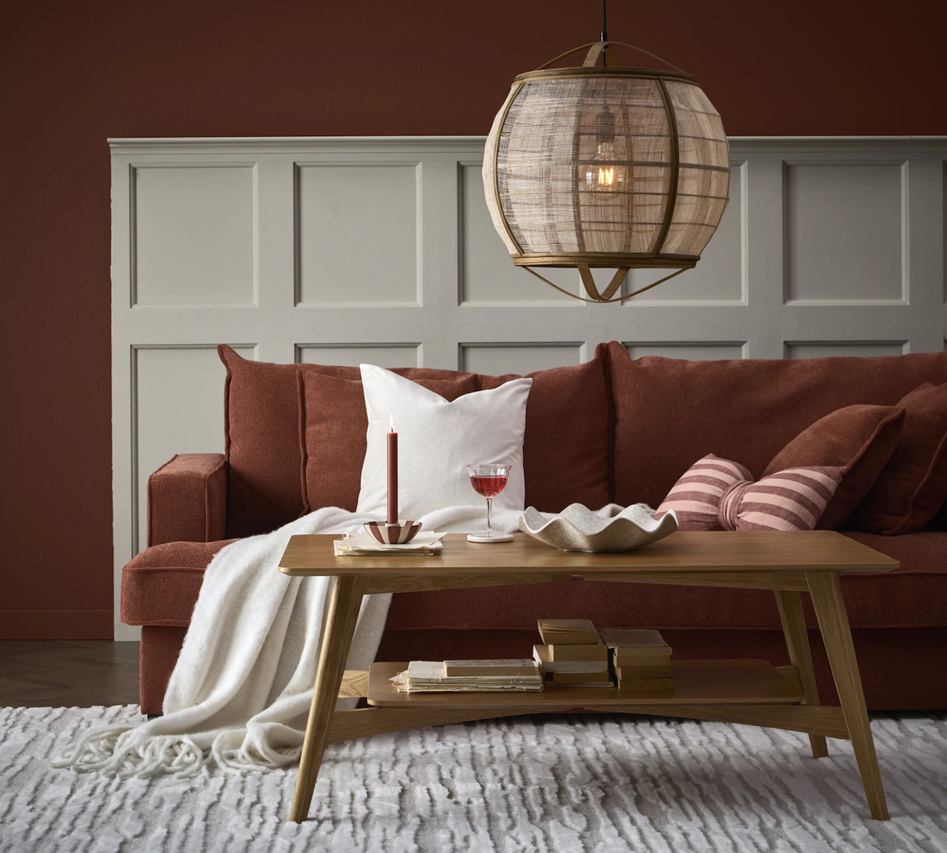 I ett vardagsrum står en roströd Mila soffa bakom ett soffbord i ek