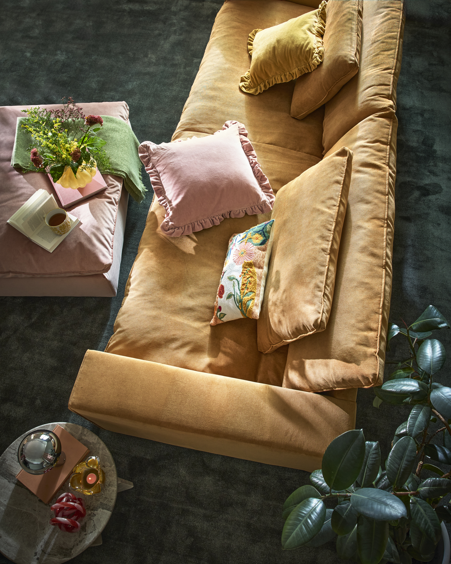 En djup ockragul soffa sedd ovanifrån, i ett murrigt vardagsrum med härliga färgklickar i dekor och textilier