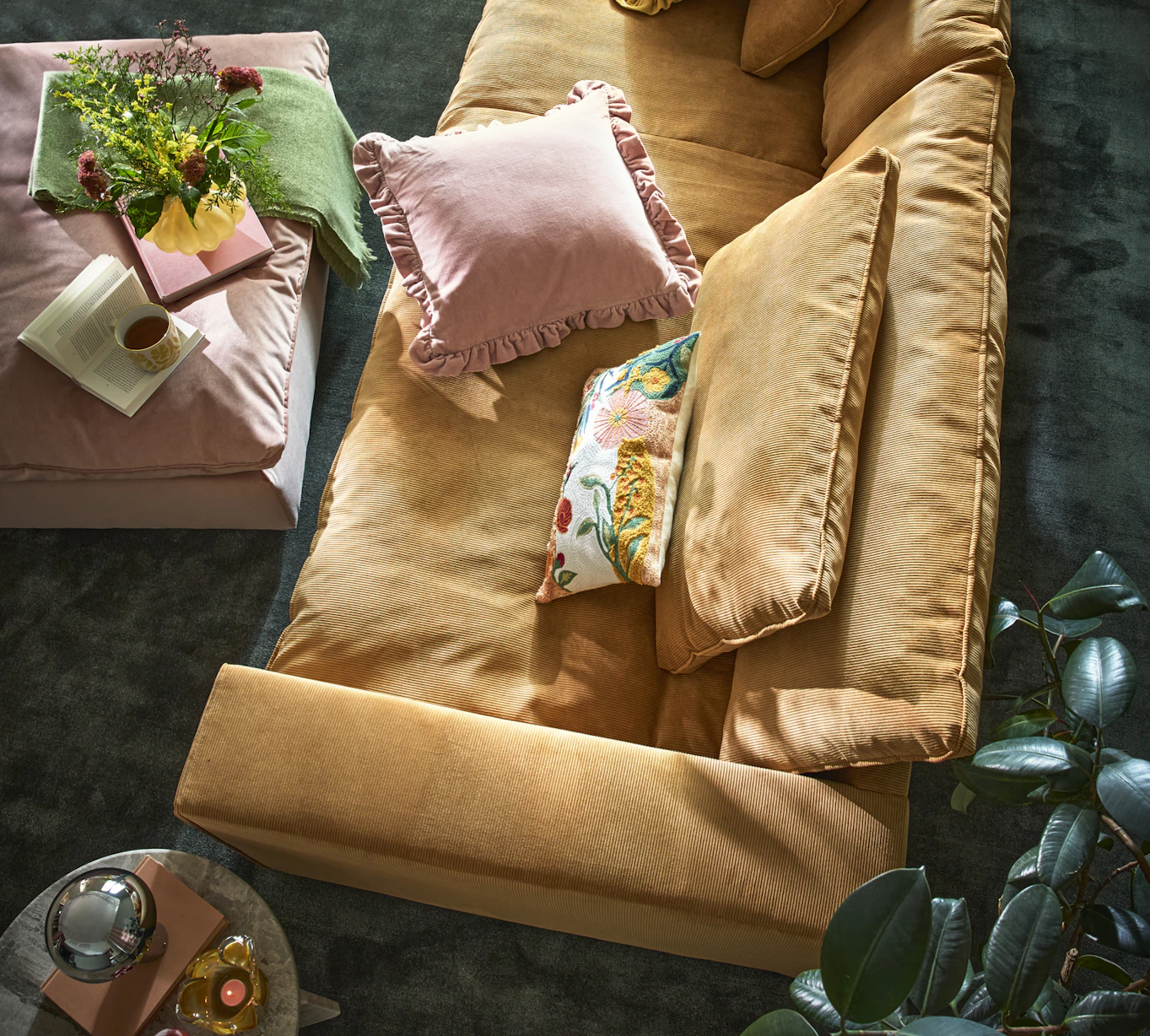 En djup ockragul soffa sedd ovanifrån, i ett murrigt vardagsrum med härliga färgklickar i dekor och textilier