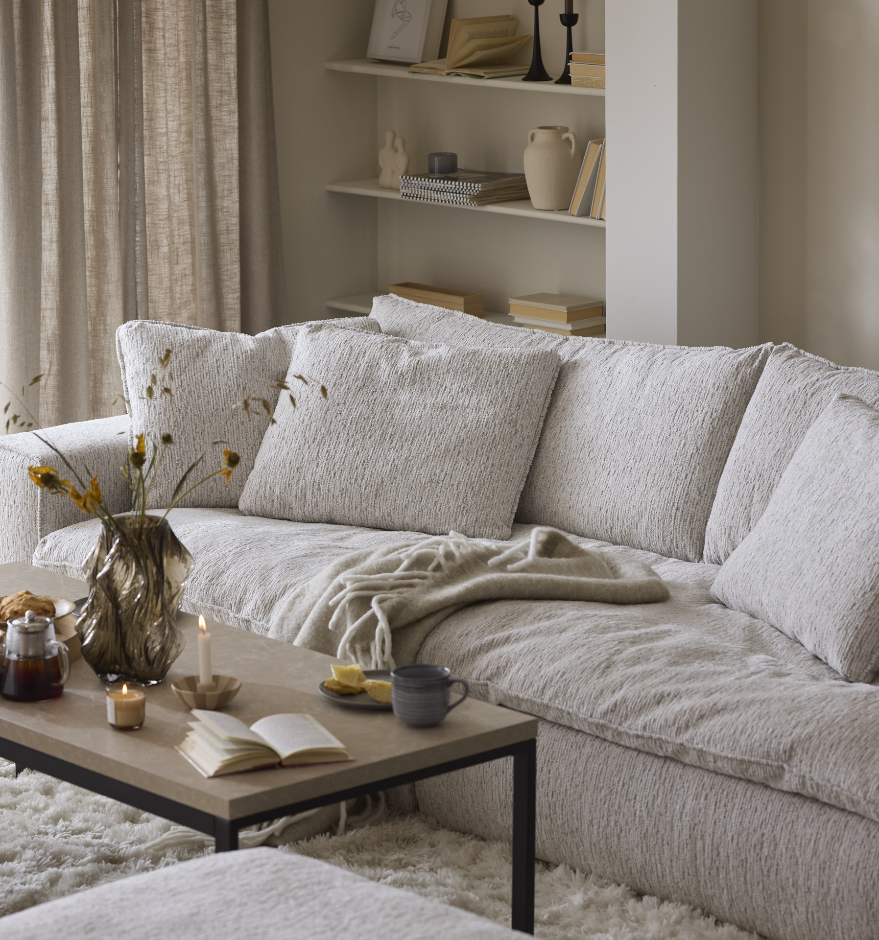 En ljus, djup soffa står i ett beige vardagsrum bakom ett soffbord i trä