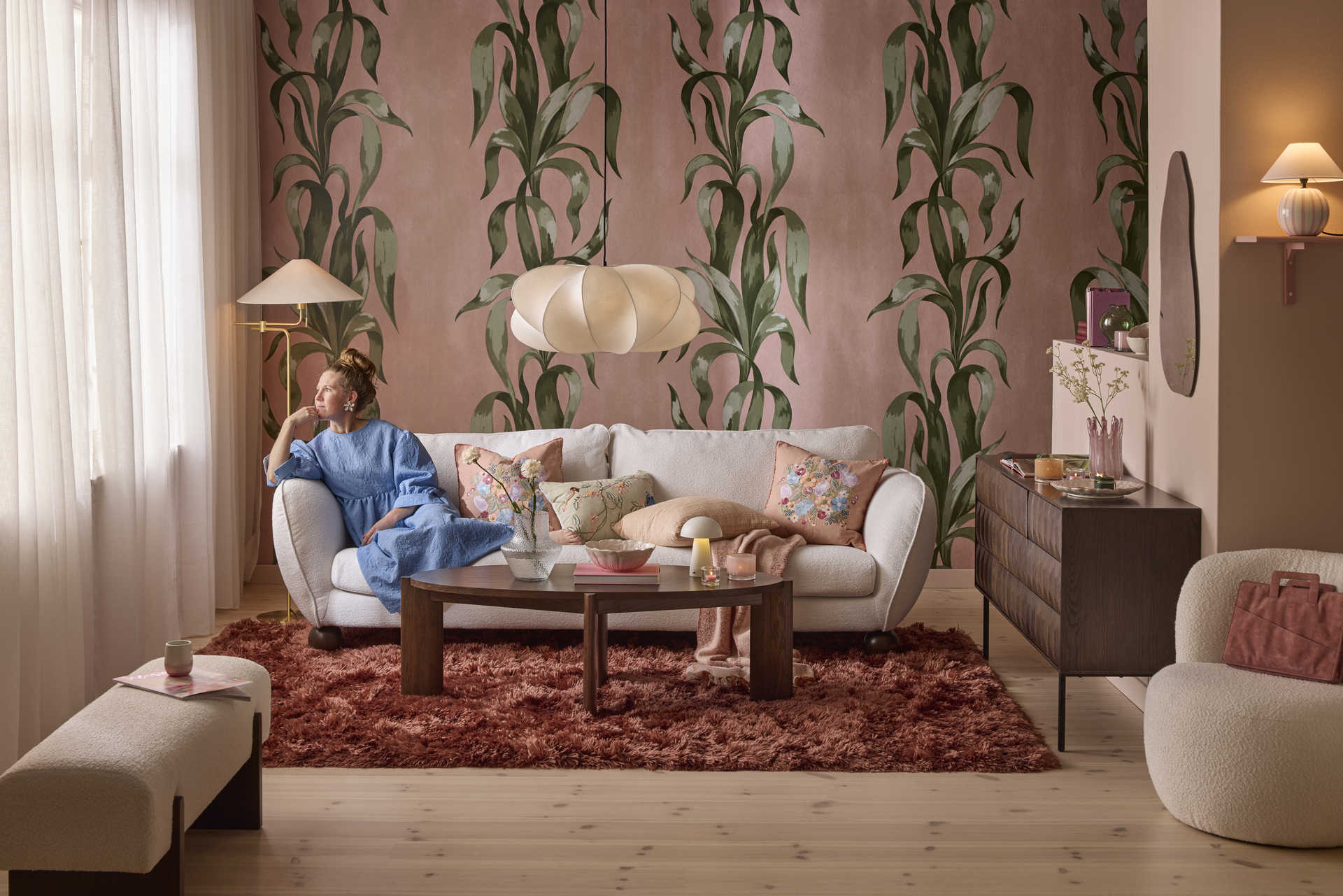 En Madison-soffa med runda, bulliga former i trendig stil står i ett rosa vardagsrum. En kvinna lutar sig mot armstödet