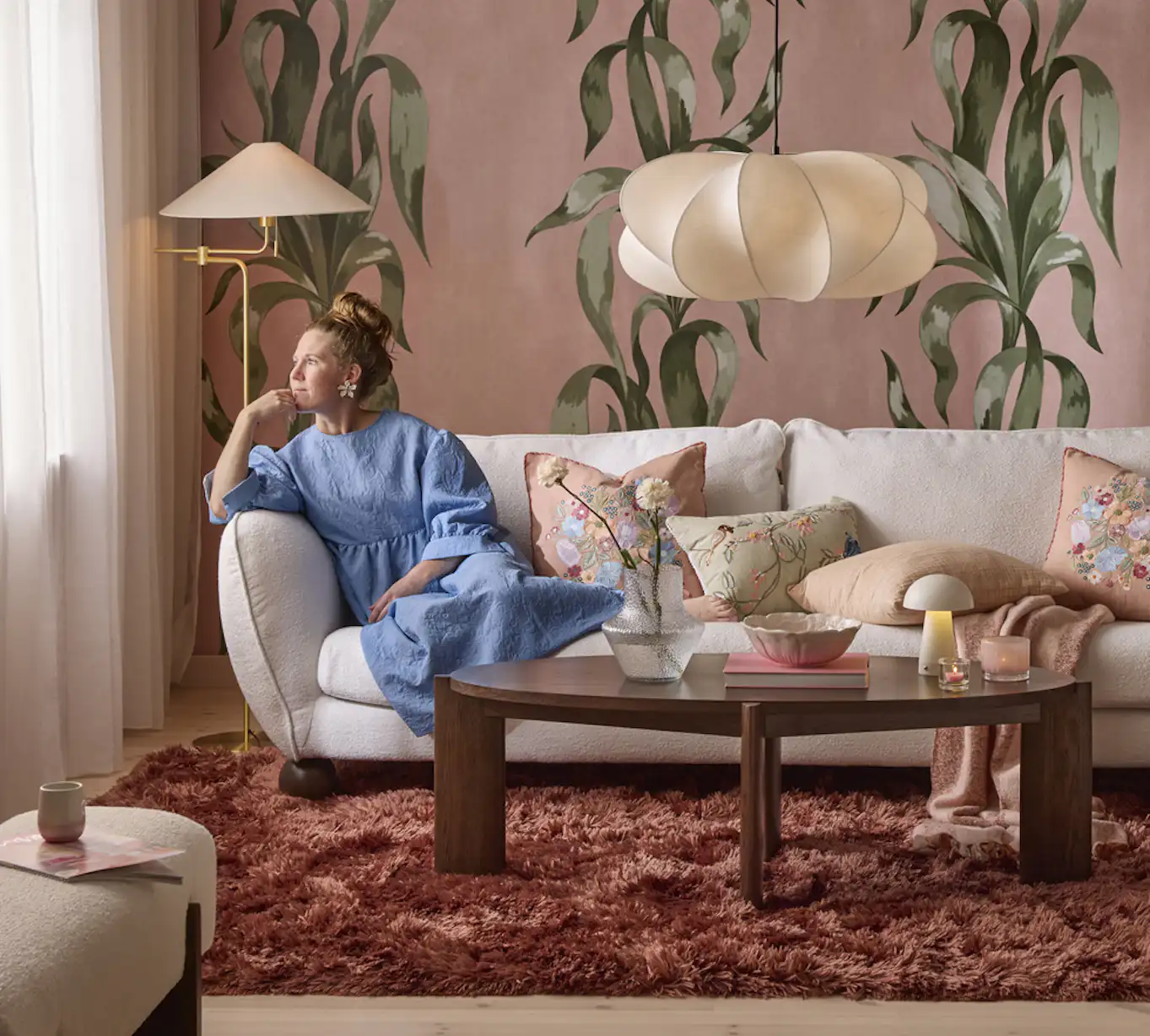 En Madison-soffa med runda, bulliga former i trendig stil står i ett rosa vardagsrum. En kvinna lutar sig mot armstödet