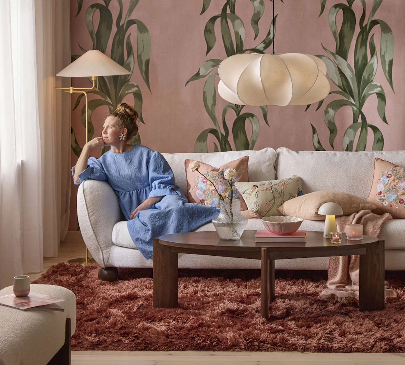 En Madison-soffa med runda, bulliga former i trendig stil står i ett rosa vardagsrum. En kvinna lutar sig mot armstödet