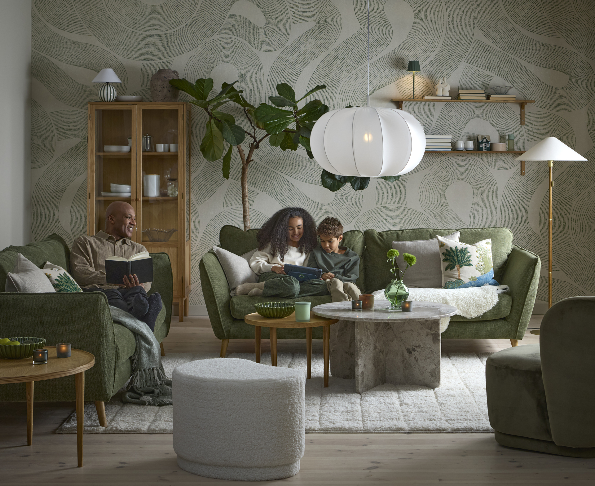 I ett vardagsrum i gröna toner sitter två barn och läser i en grön Madison soffa