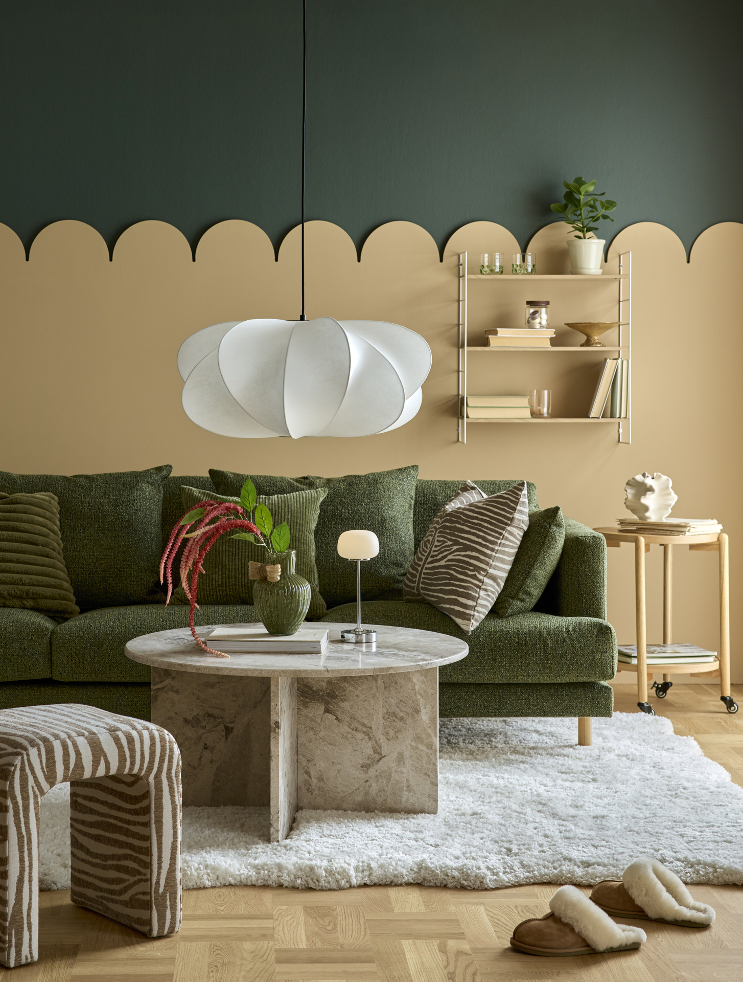 I ett lekfullt inrett vardagsrum står en mossgrön soffa bakom ett soffbord i marmor