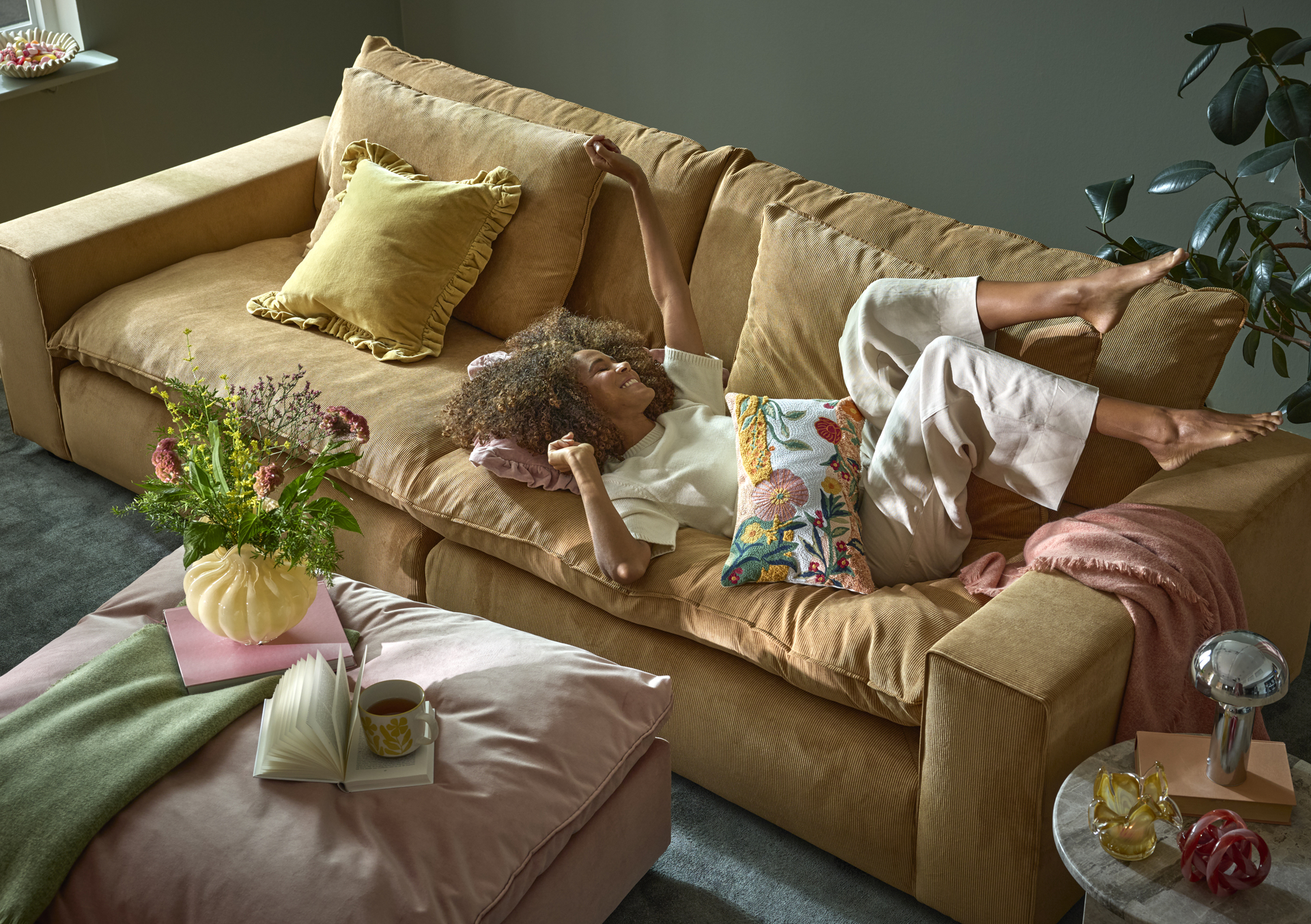 En kvinna ligger i en djup, ockrsgul soffa i sammet