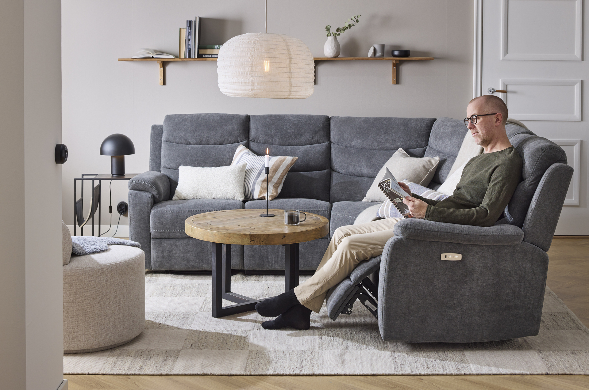 I en grå hörnsoffa med reclinerfunktion sitter en man och läser
