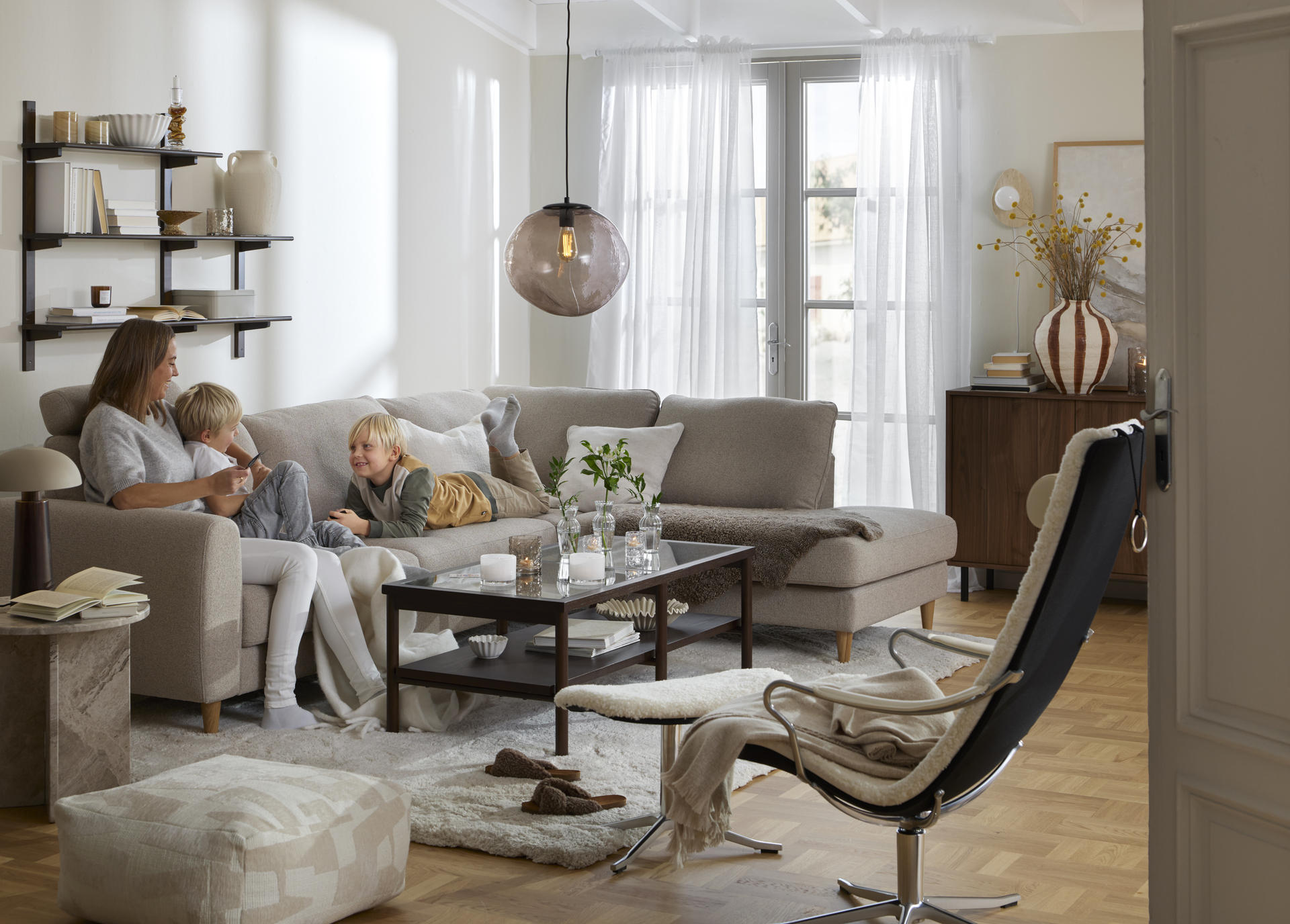 I en beige divansoffa sitter en kvinna och två barn