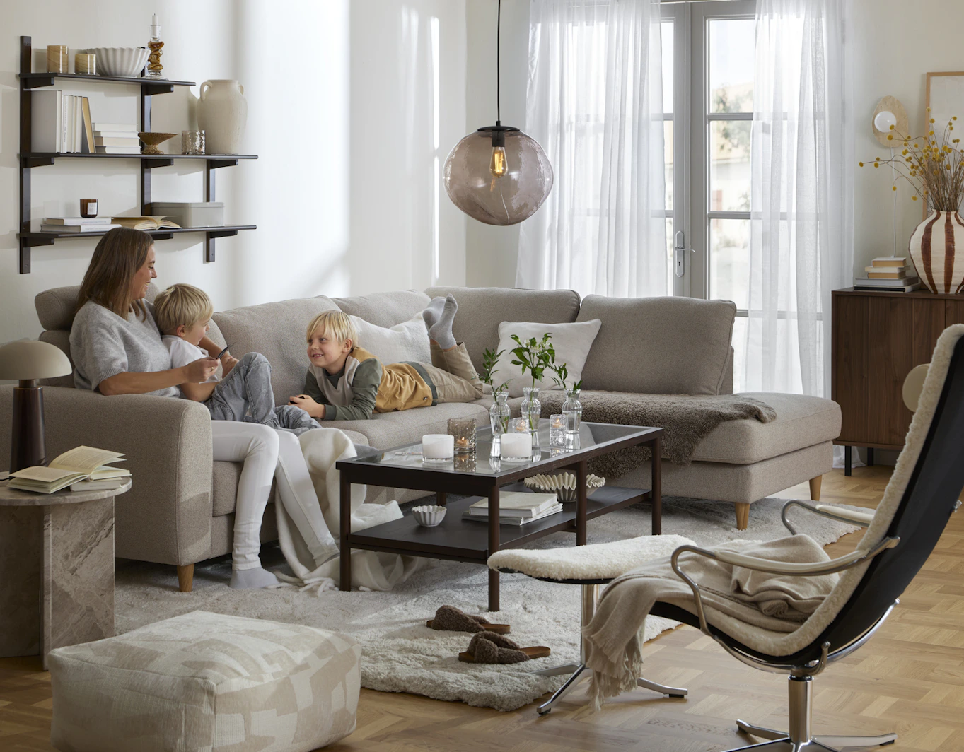 I en beige divansoffa sitter en kvinna och två barn