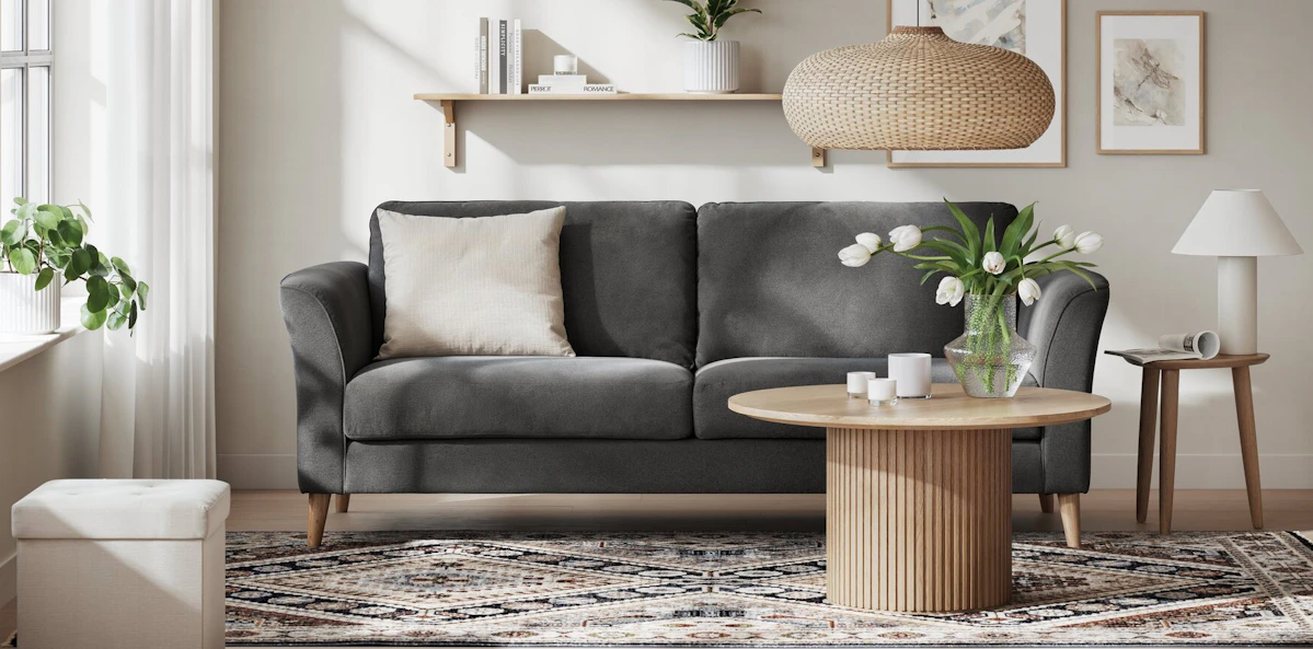 I ett stilrent vardagsrum står en mörkgrå soffa bakom ett soffbord i ek