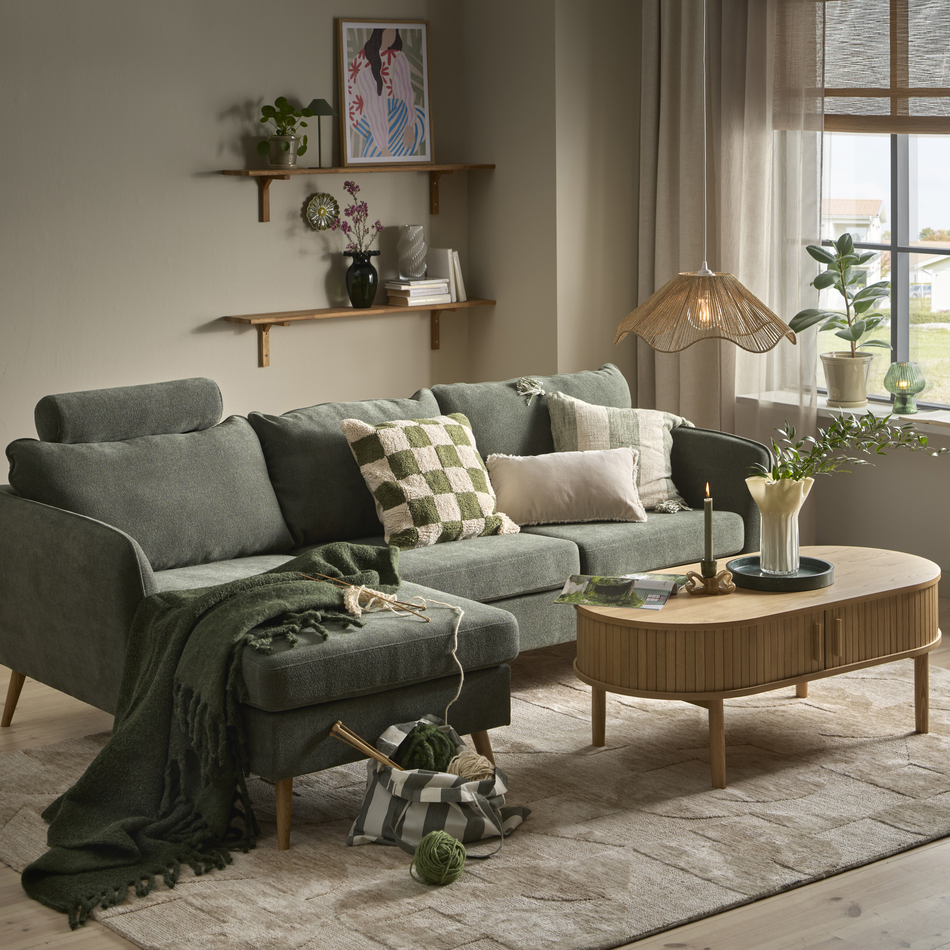 I ett stilrent vardagsrum står en grön soffa med schäslong bakom ett soffbord i ljust trä