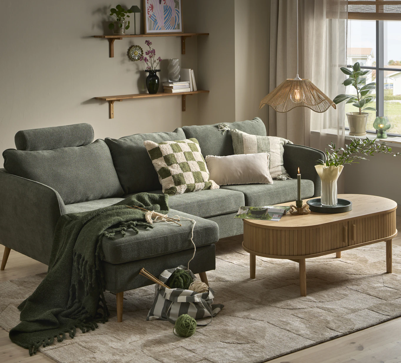 I ett stilrent vardagsrum står en grön soffa med schäslong bakom ett soffbord i ljust trä