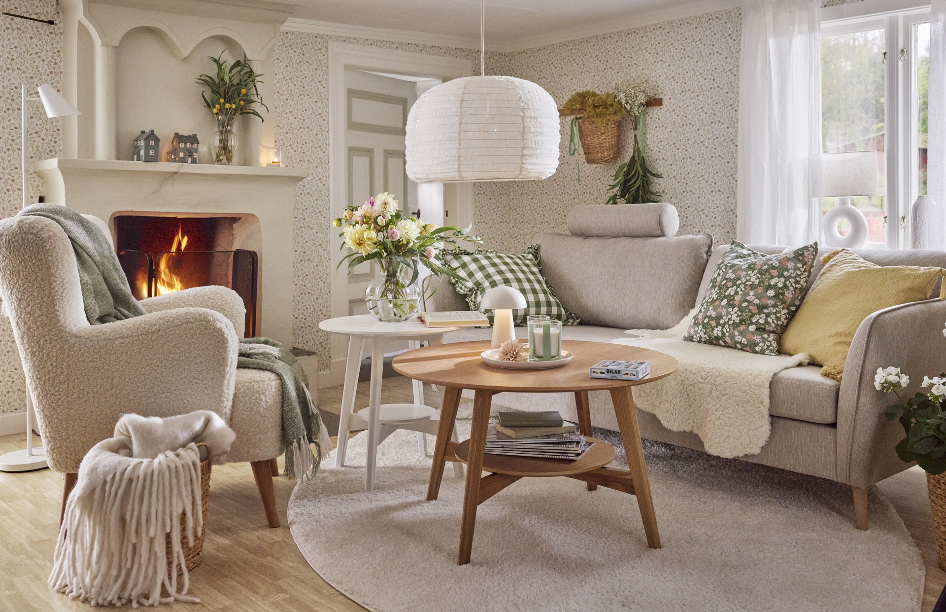 I ett lantligt vardagsrum med blommig tapet står en ljusgrå soffa