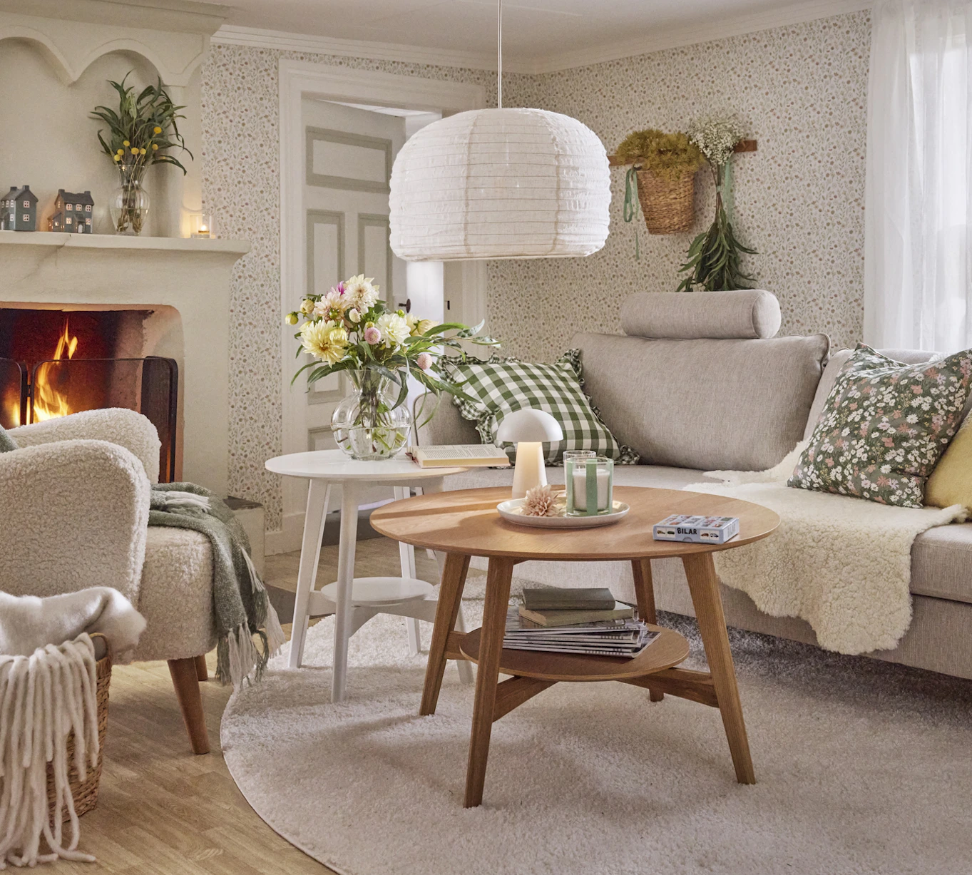 I ett lantligt vardagsrum med blommig tapet står en ljusgrå soffa