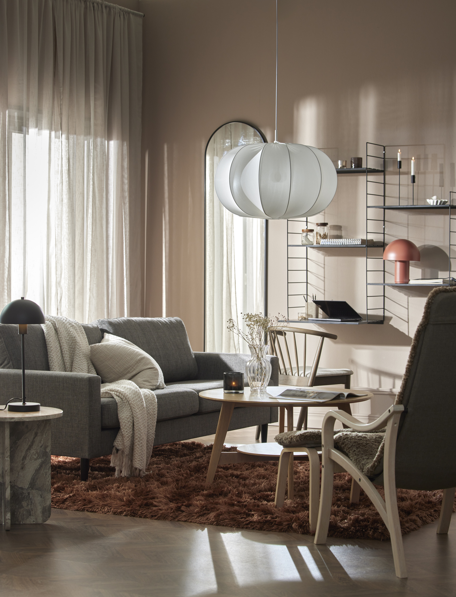 I ett vardagsrum i rosa toner står en grå soffa bakom ett soffbord i ljust trä