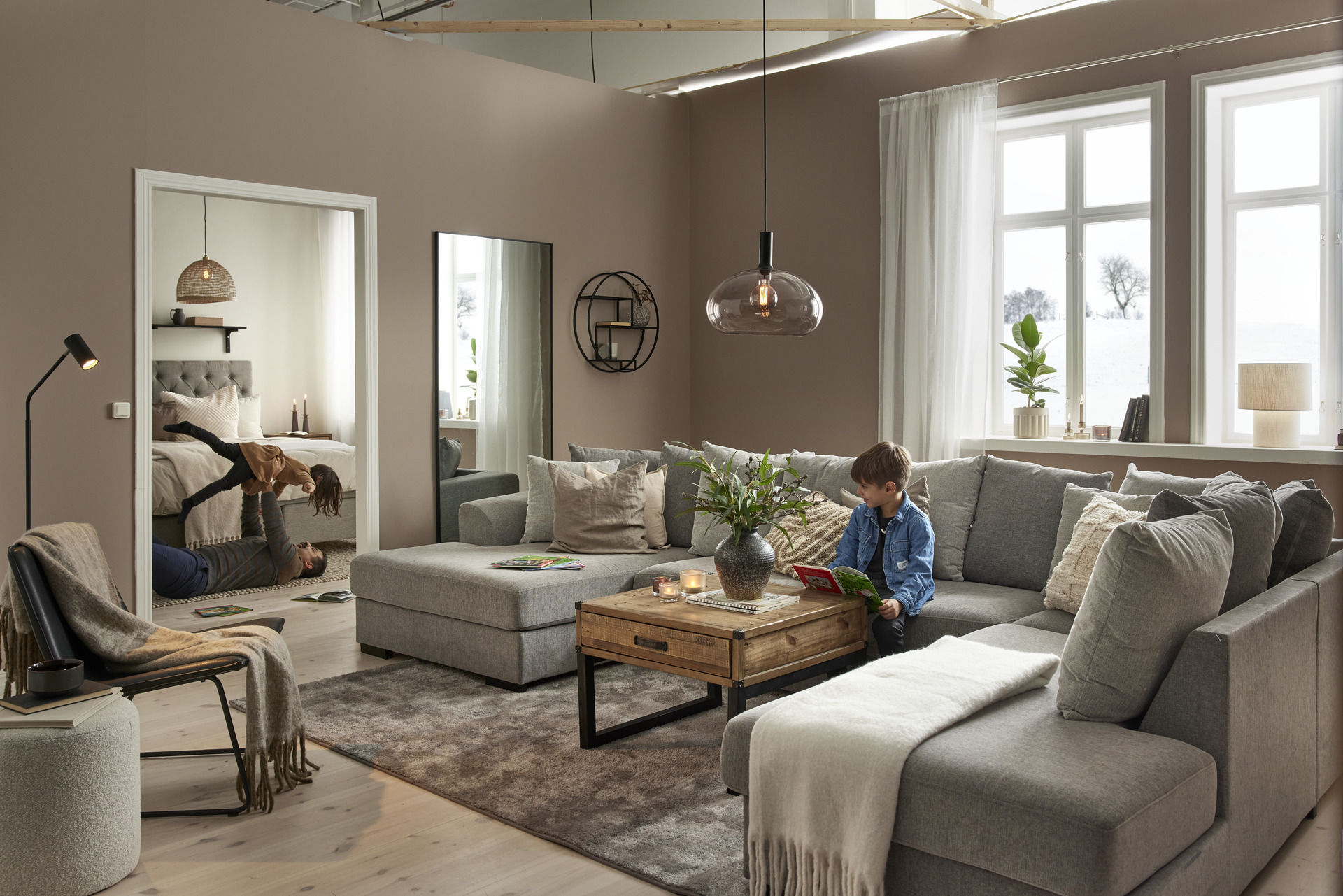 I ett vardagsrum står en stor, grå u-soffa, i soffan sitter en pojke och läser