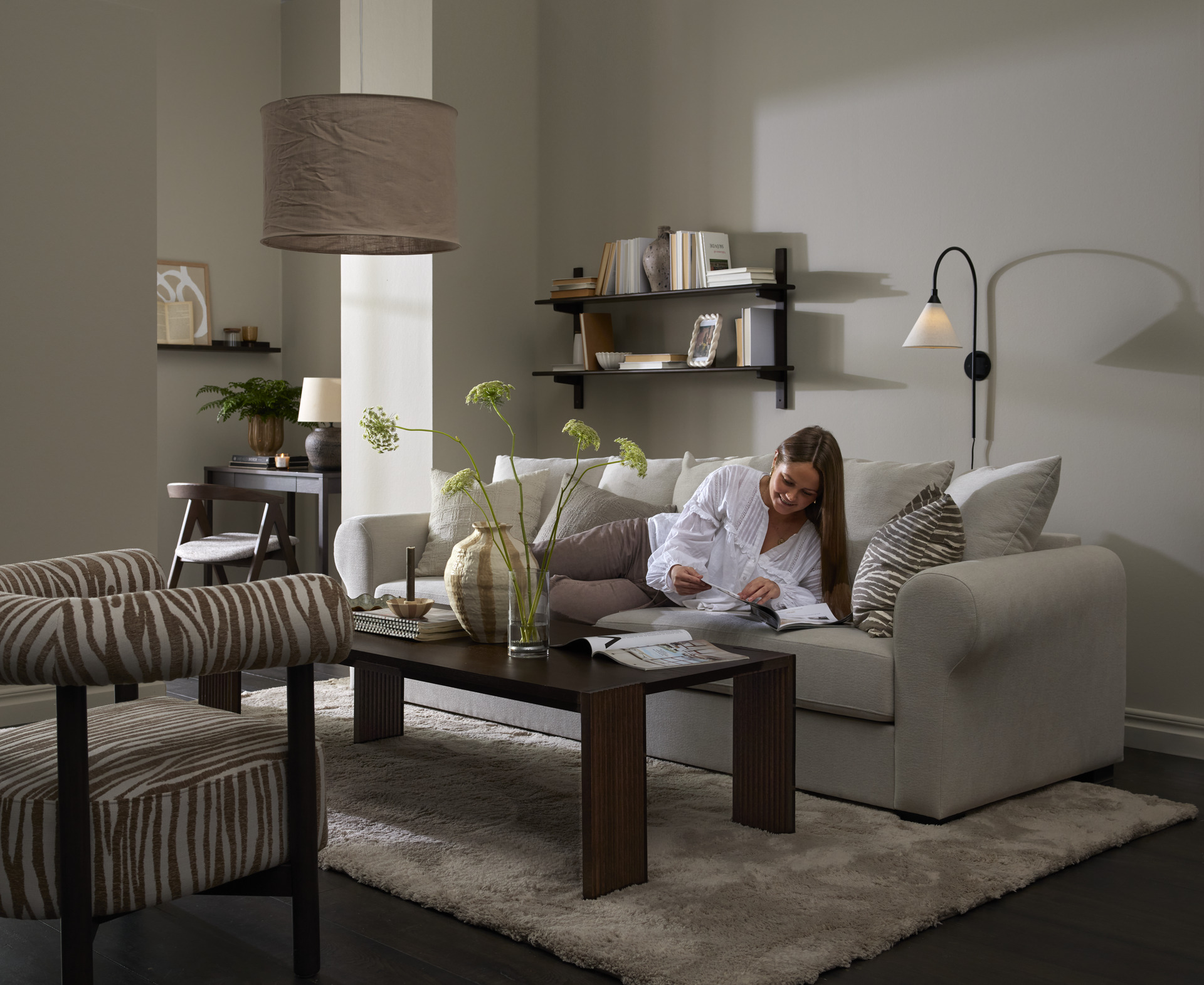I ett stilrent vardagsrum ligger en kvinna och läser i en vit soffa