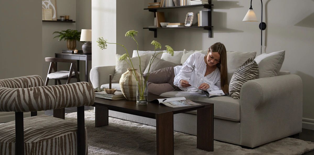I ett stilrent vardagsrum ligger en kvinna och läser i en vit soffa