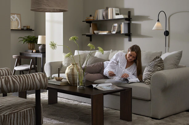 I ett stilrent vardagsrum ligger en kvinna och läser i en vit soffa