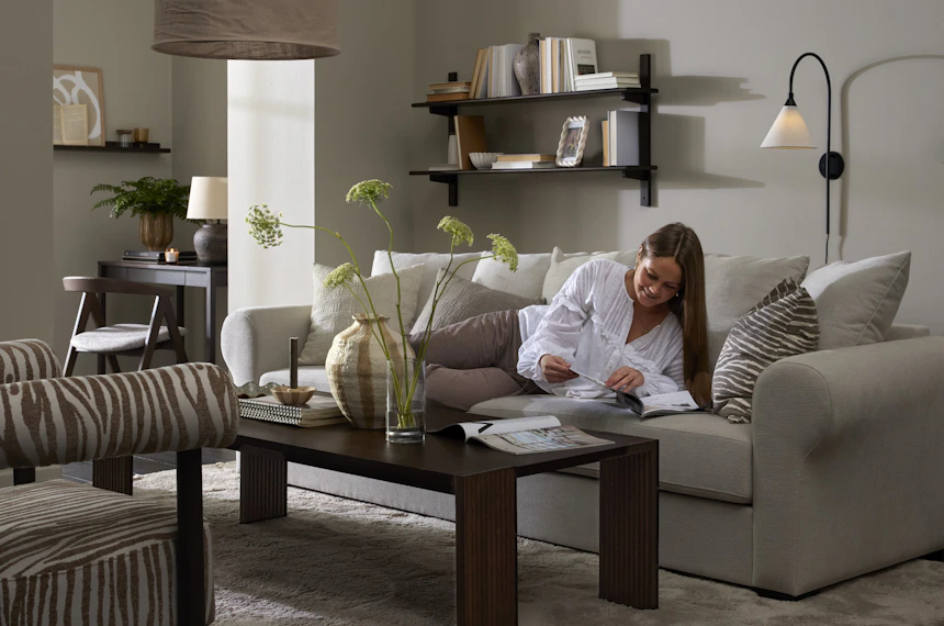 I ett stilrent vardagsrum ligger en kvinna och läser i en vit soffa